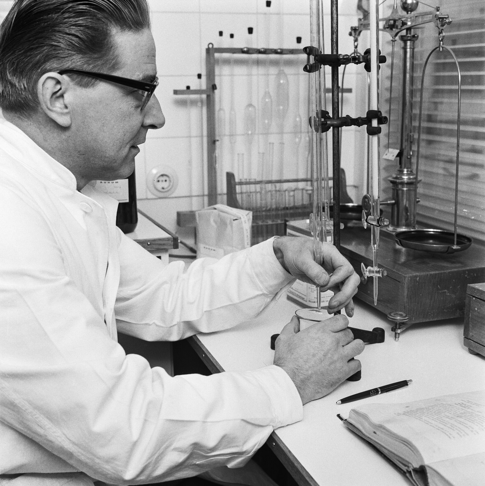 Pharmacist in a white coat titrating a sample with a burette, next to a precision balance, in 1965